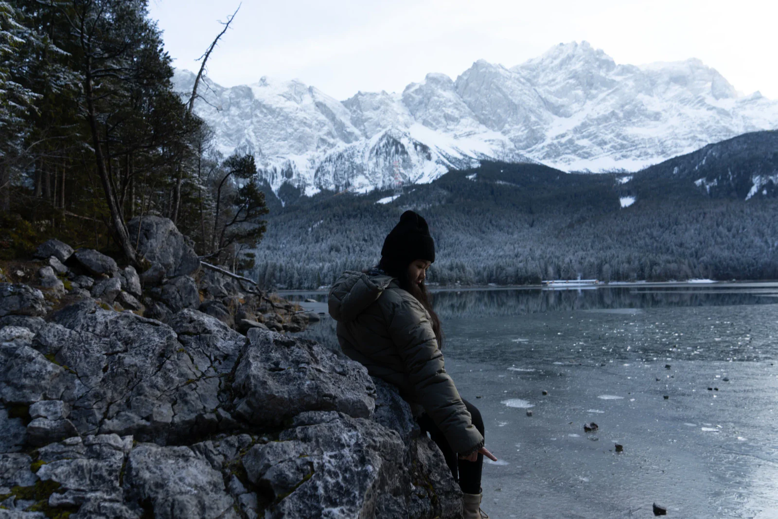 Person blickt an einem winterlichen Bergsee auf die verschneiten Alpen