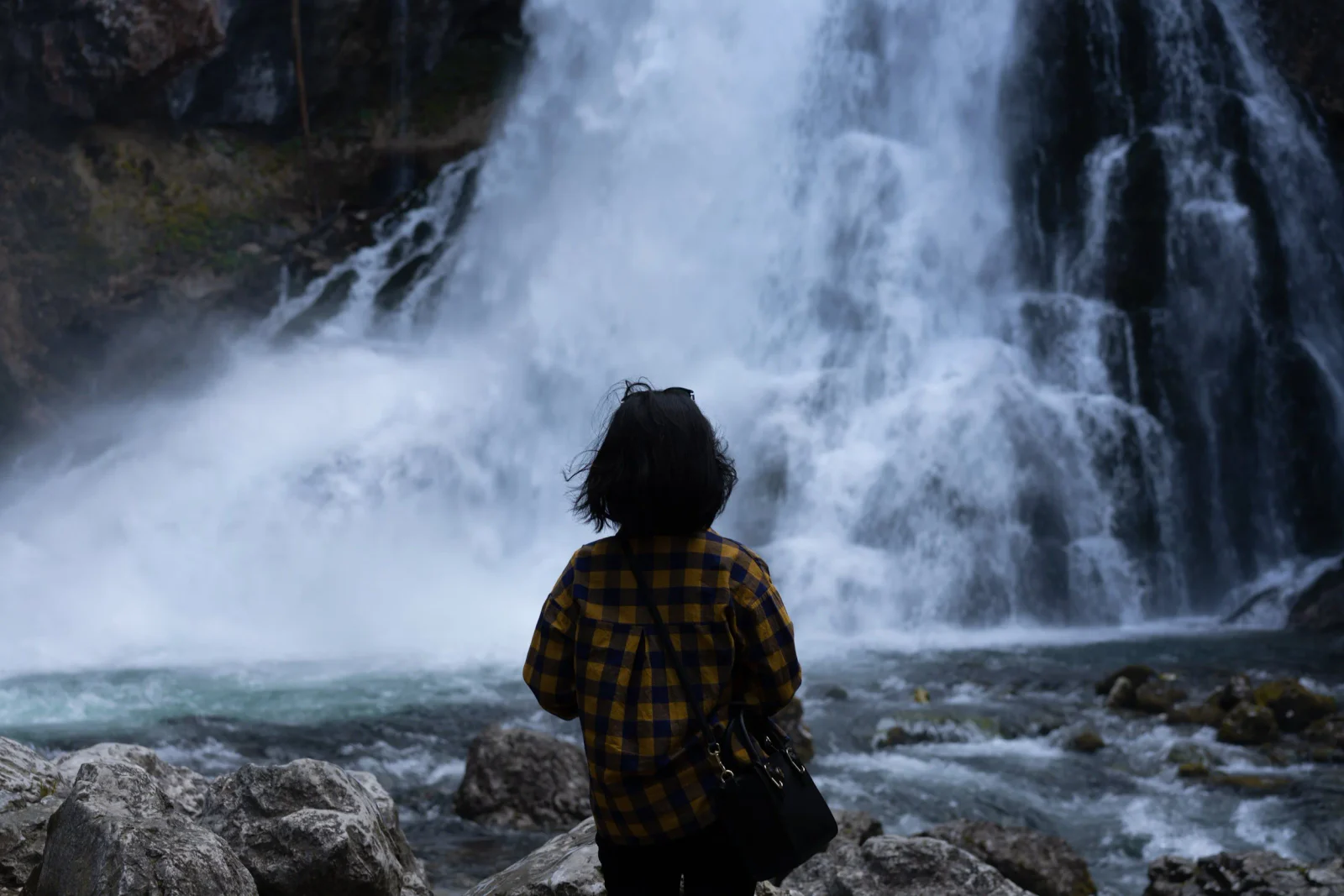Person steht vor einem kraftvollen Wasserfall in den Bergen