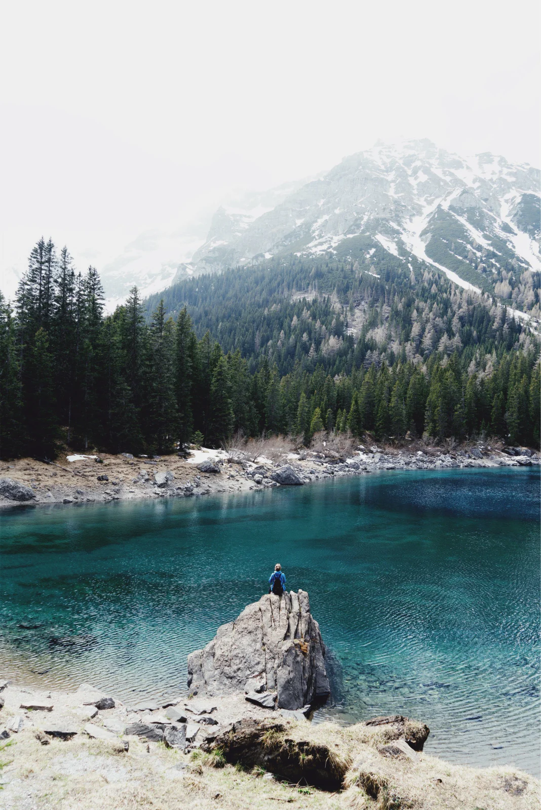 Türkisfarbener Bergsee mit Felsen und verschneitem Gebirge