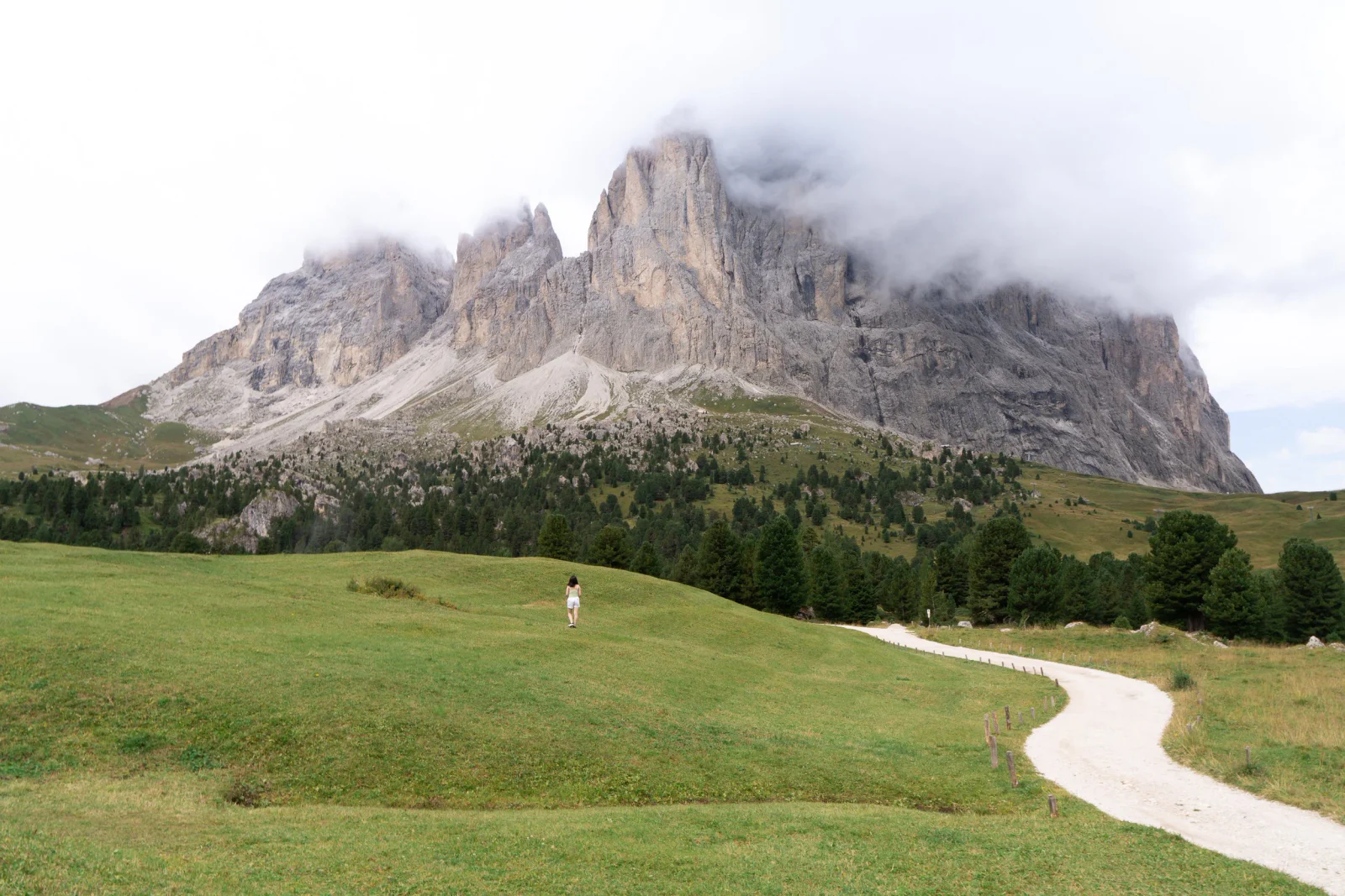 Weite Berglandschaft mit einer Wanderin unter markanten Felsgipfeln