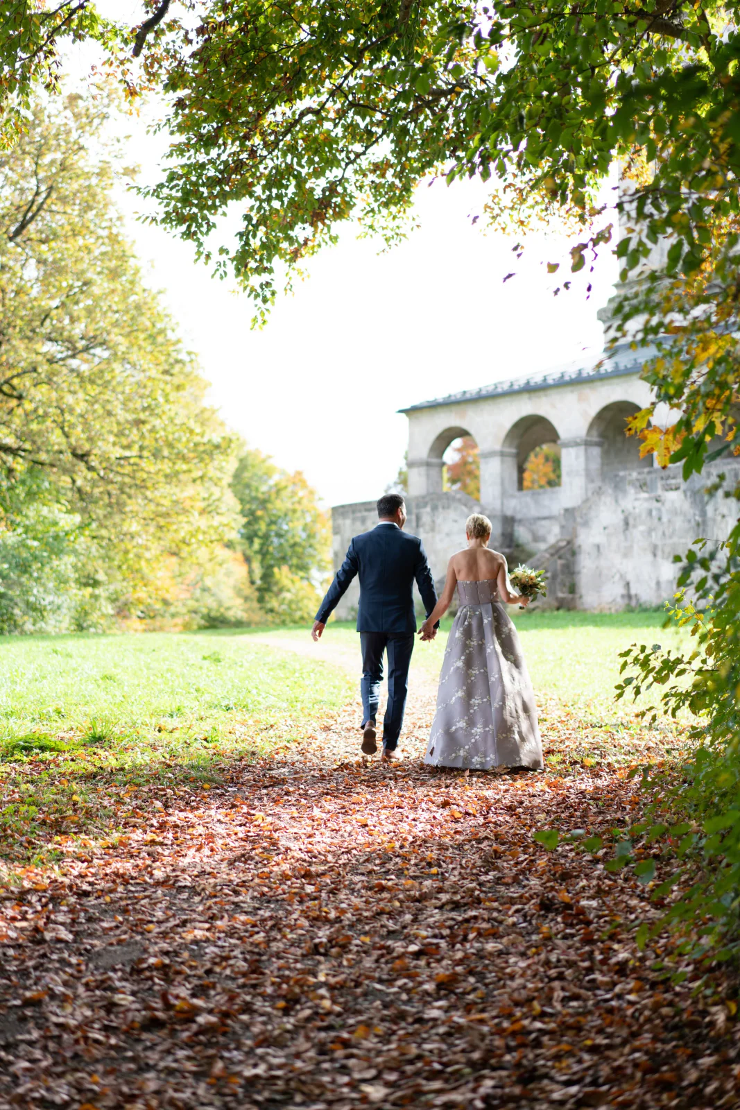 Brautpaar geht Hand in Hand durch einen herbstlichen Schlosspark