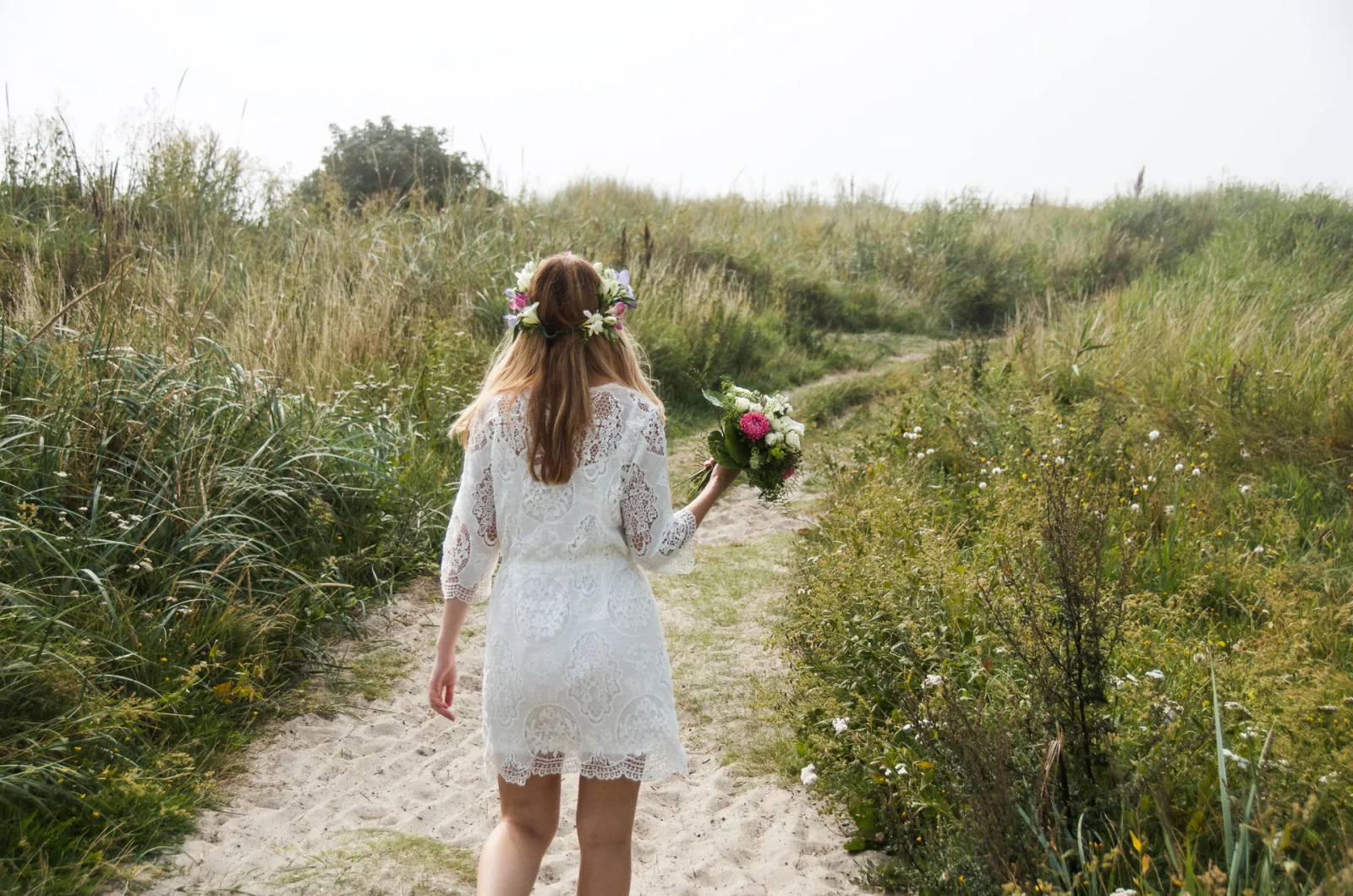 Braut mit Blumenkranz und Brautstrauß auf einem Weg durch die Natur