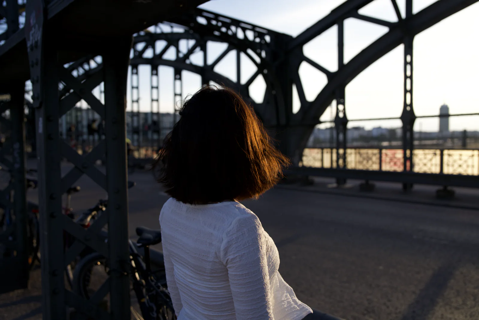 Frau im hellen Oberteil mit dem Rücken zur Kamera auf einer Stahlbrücke im Abendlicht