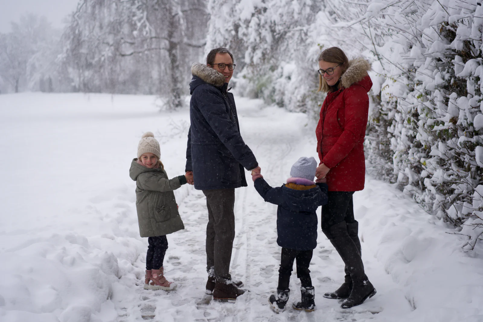 Zwei Erwachsene und zwei Kinder halten sich auf einem verschneiten Weg an den Händen