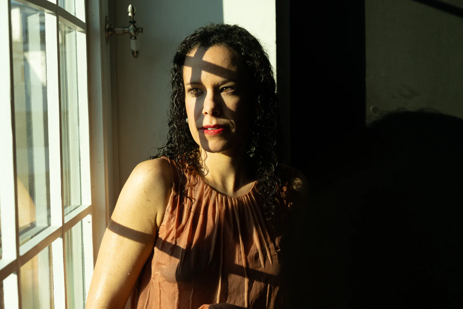 Frau mit nassem lockigem Haar im geometrischen Schatten eines Sprossenfensters