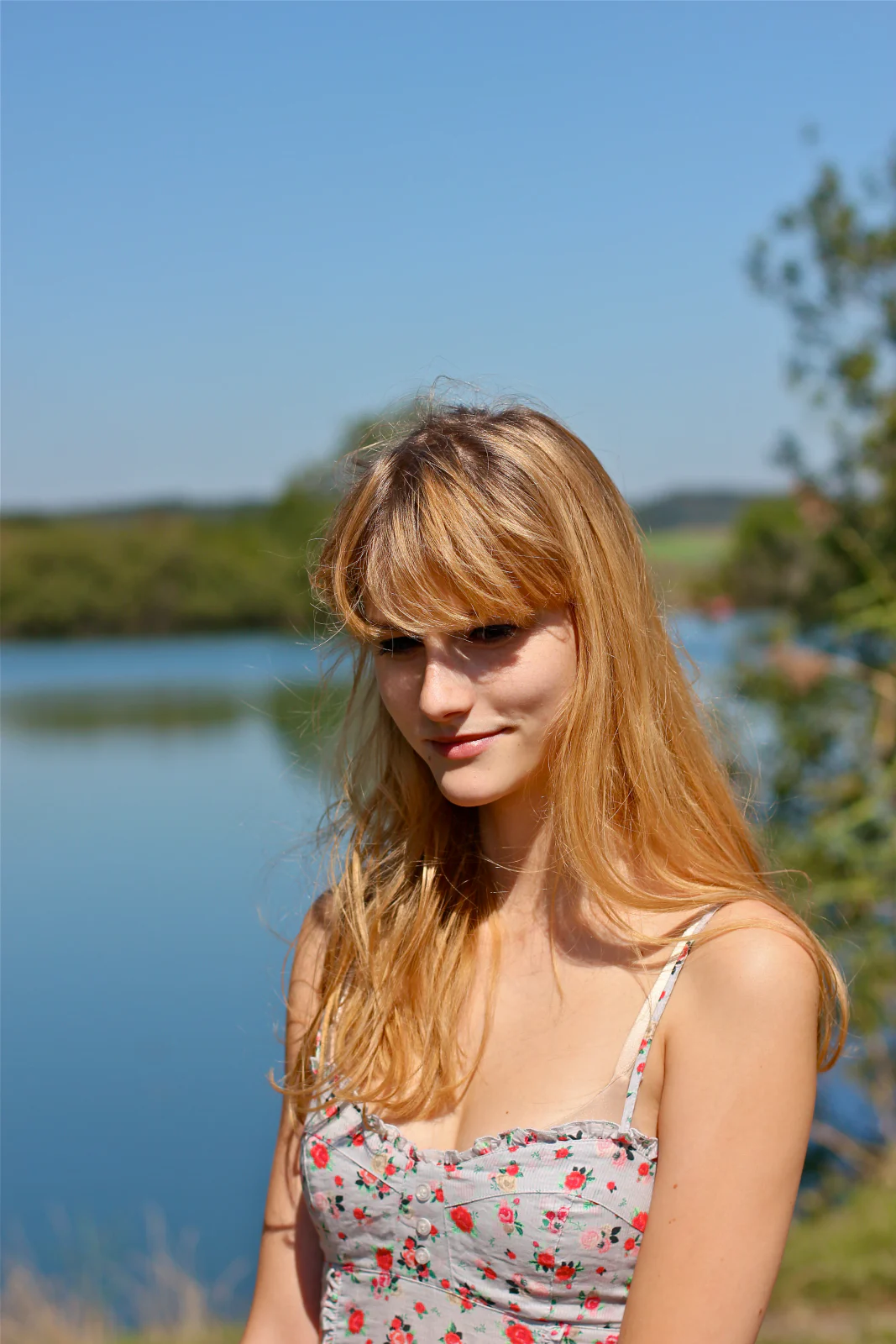 Junge Frau im geblümten Kleid vor einem ruhigen See und blauem Himmel
