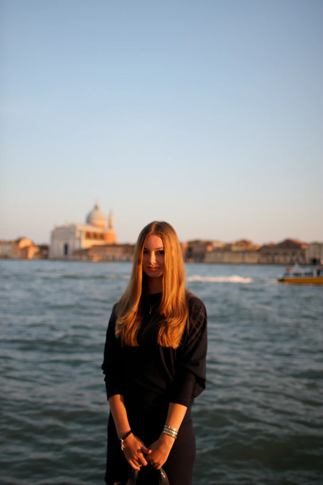 Junge Frau in schwarzer Kleidung am Wasser vor der historischen Stadtsilhouette von Venedig