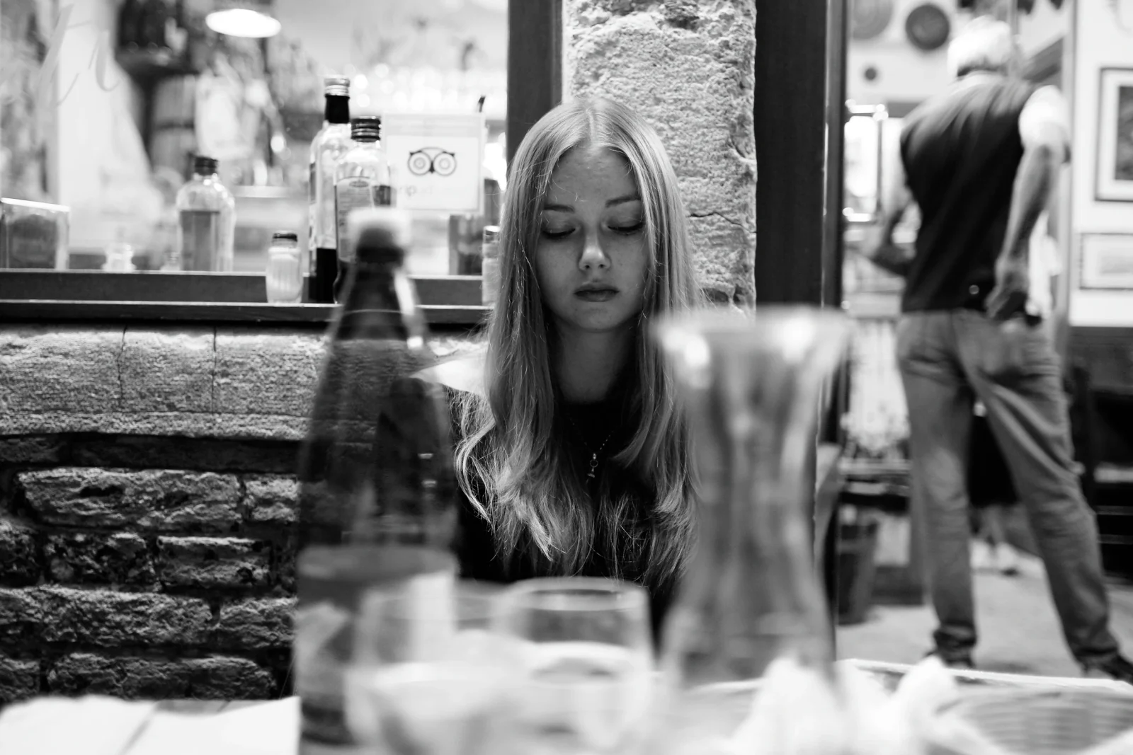 Schwarz-Weiß-Portrait einer jungen Frau am Restauranttisch durch Gläser im Vordergrund