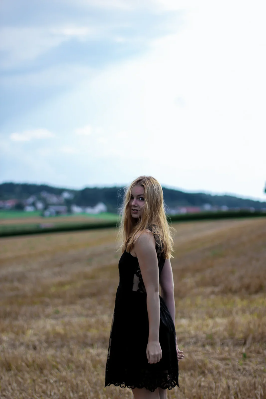 Junge Frau in schwarzem Kleid auf einem abgeernteten Feld unter hellem Himmel